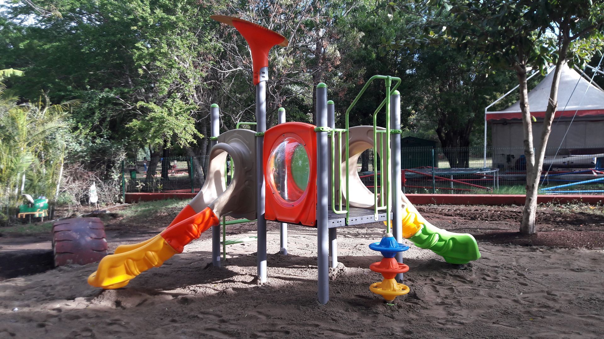 Aire de jeux colorée avec toboggans, panneaux d'escalade et jeu à ressort dans un parc ombragé