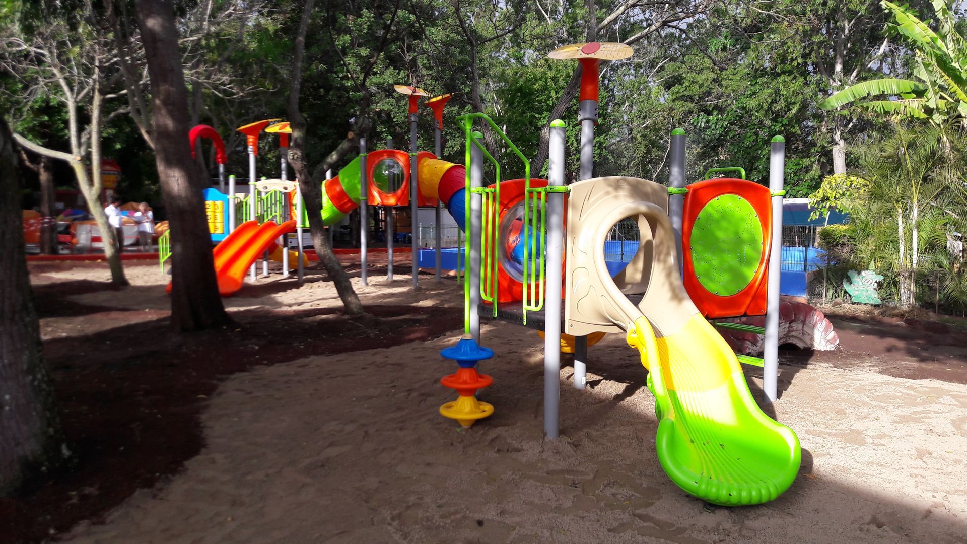 Aire de jeux colorée avec toboggans, tunnels d'escalade et balançoire sous les arbres