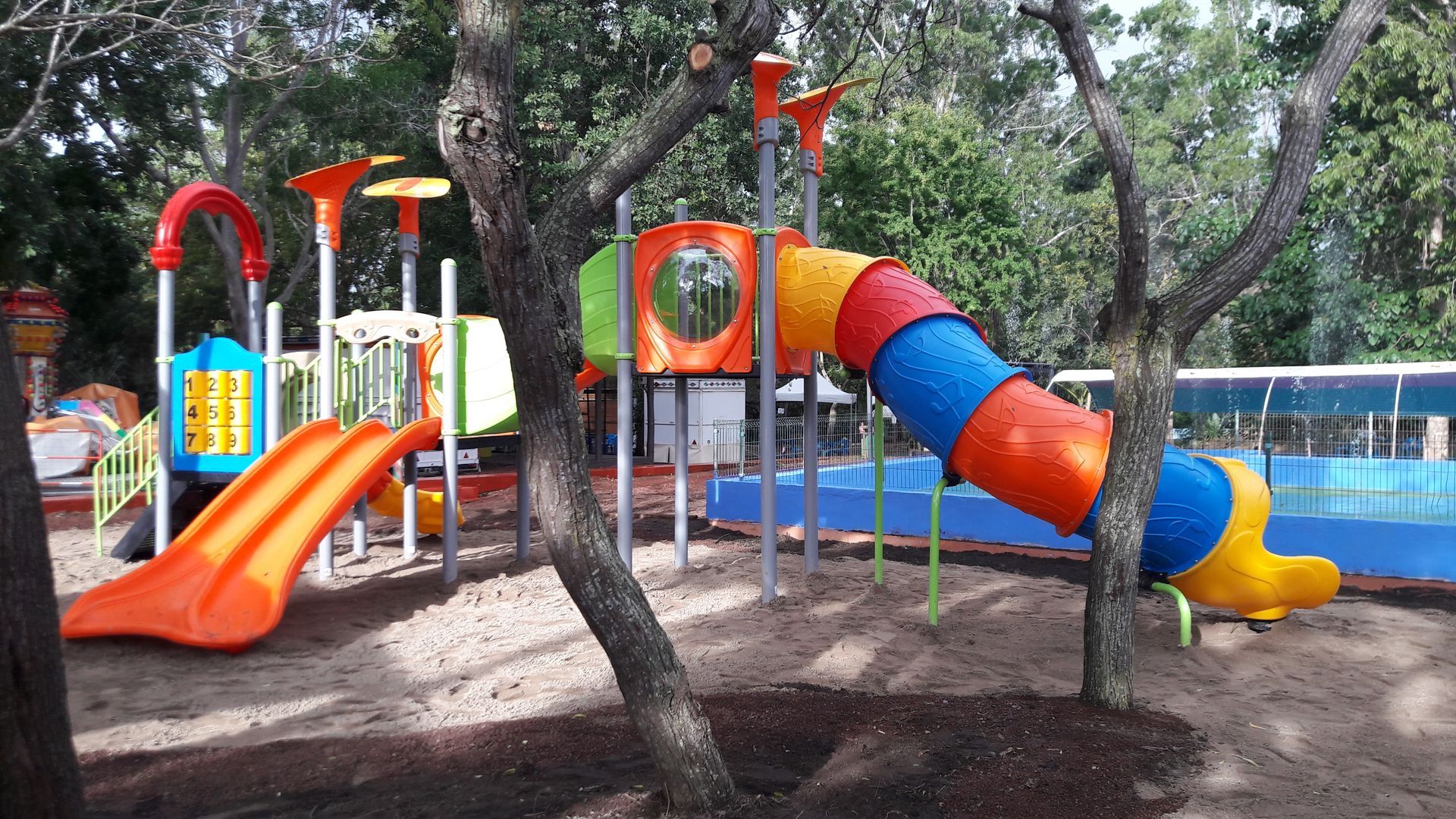 Aire de jeux colorée avec toboggans et tunnel d'escalade au milieu des arbres d'un parc