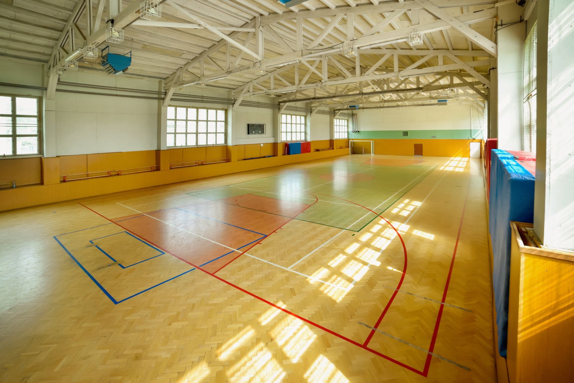 Gymnase intérieur vide avec parquet ciré, lignes de terrain et lumière du soleil filtrant à travers les fenêtres