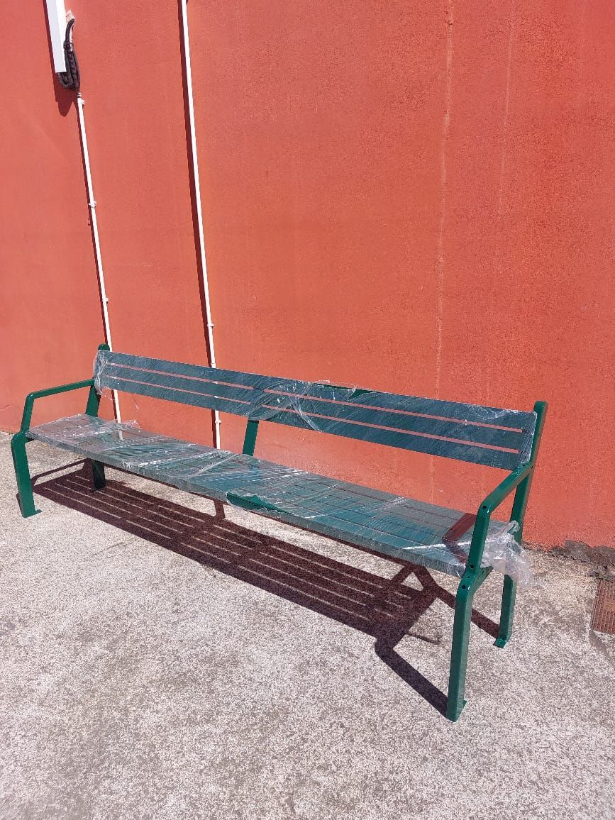 Banc en métal vert contre un mur orange sur une surface gravillonnée