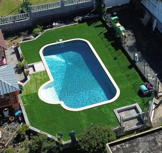 Piscine de jardin avec eau turquoise, entourée de gazon synthétique vert vif et de sièges de terrasse