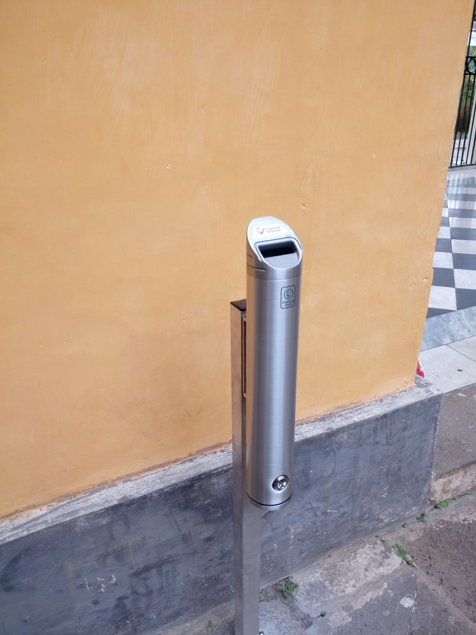 Poubelle à cendriers en acier inoxydable fixée contre un mur jaune sur un trottoir