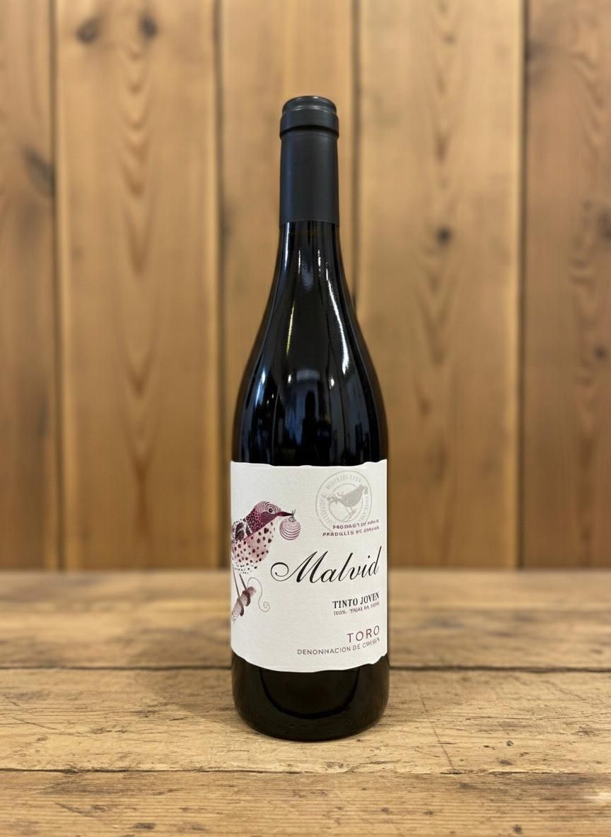 Botella de vino con etiqueta blanca, sobre una mesa de madera delante de un fondo de madera.