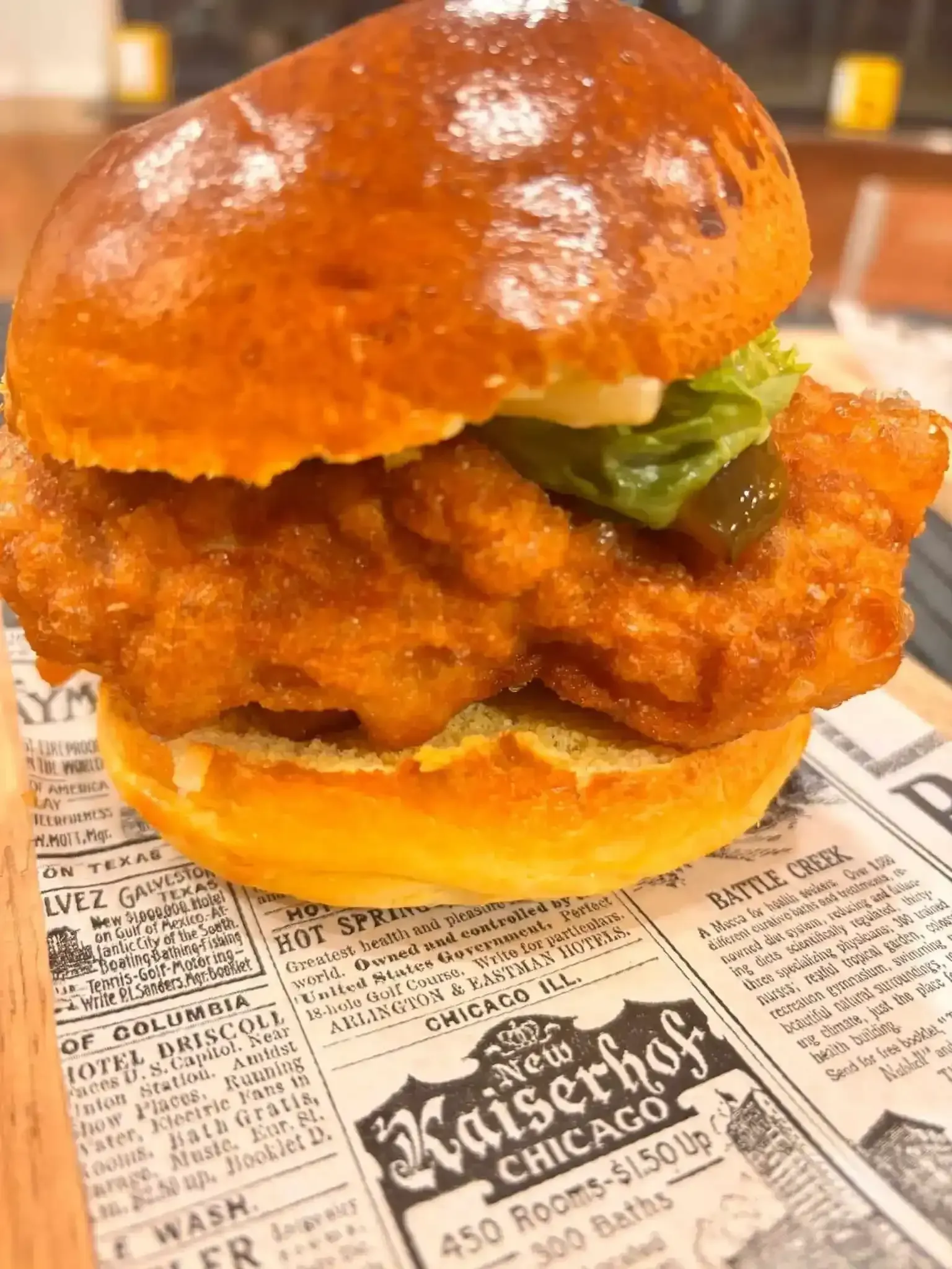 Sándwich de pollo en pan tostado con pepinillo, colocado sobre papel impreso.