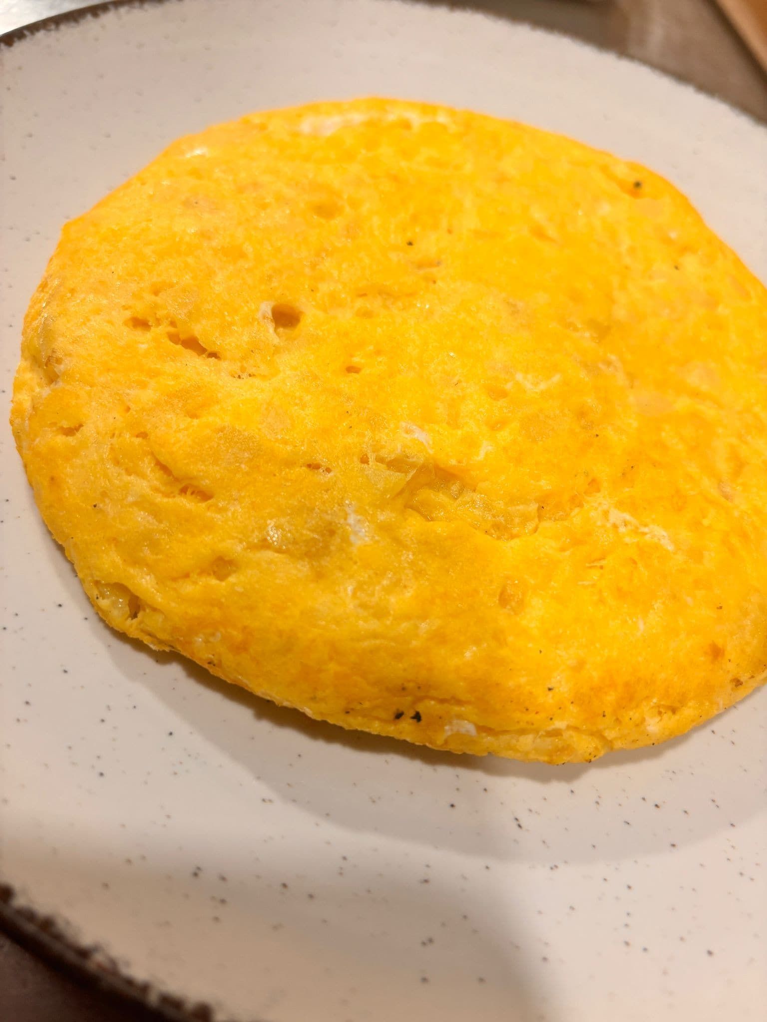 Tortilla en plato blanco, redonda y de color amarillo dorado con una textura ligeramente irregular.