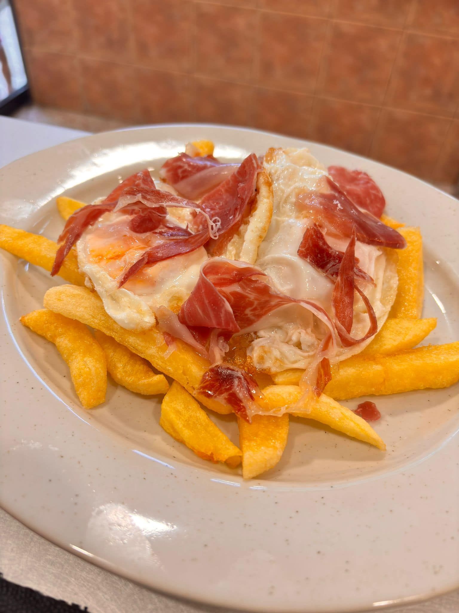 Plato de patatas fritas cubierto con un huevo frito y jamón.
