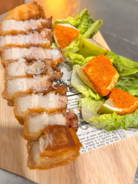 Panceta de cerdo crujiente en rodajas y tofu sazonado sobre una cama de lechuga, servido en una tabla de madera.