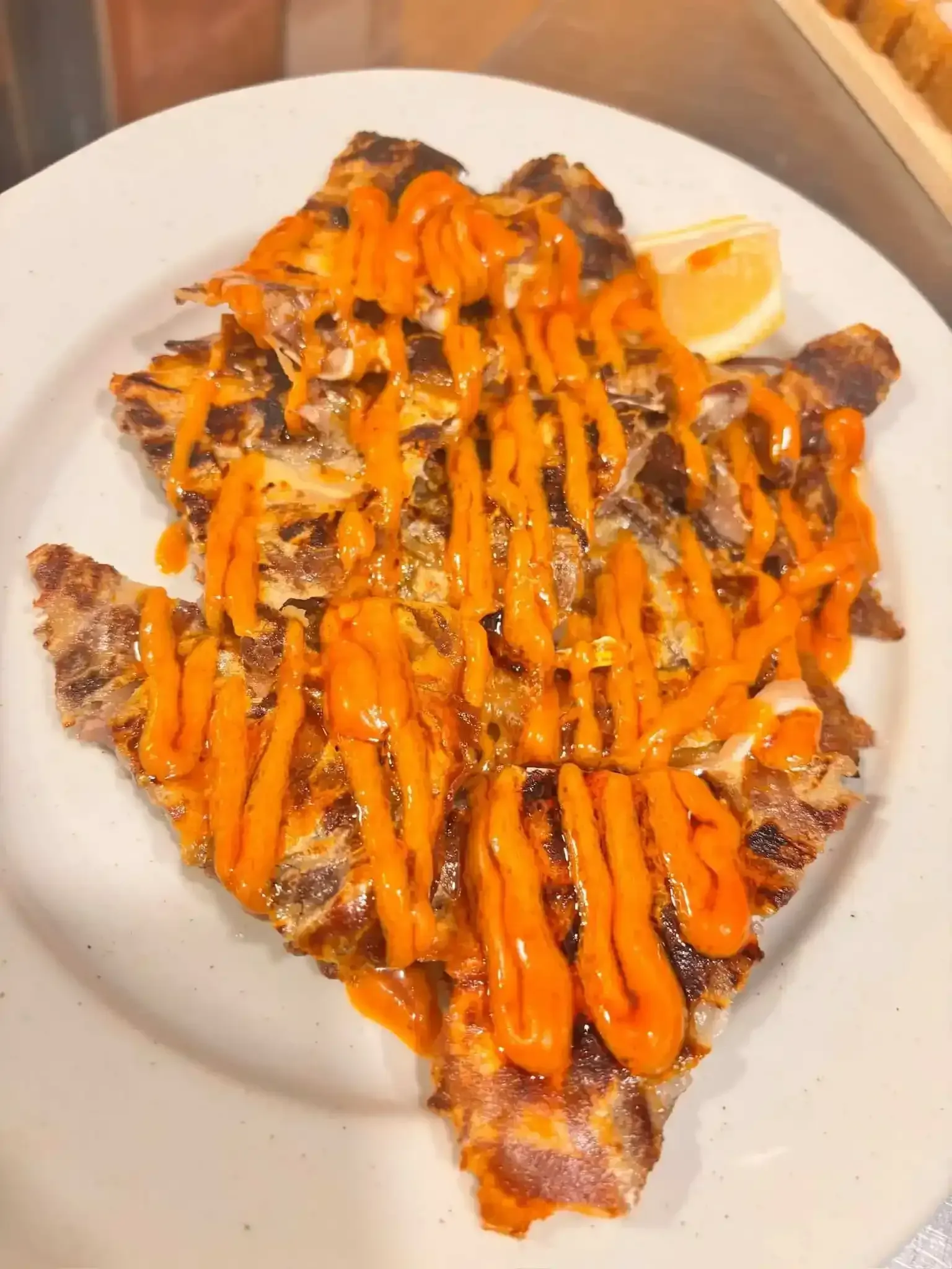 Pescado a la plancha con salsa de naranja y una rodaja de limón sobre un plato blanco.