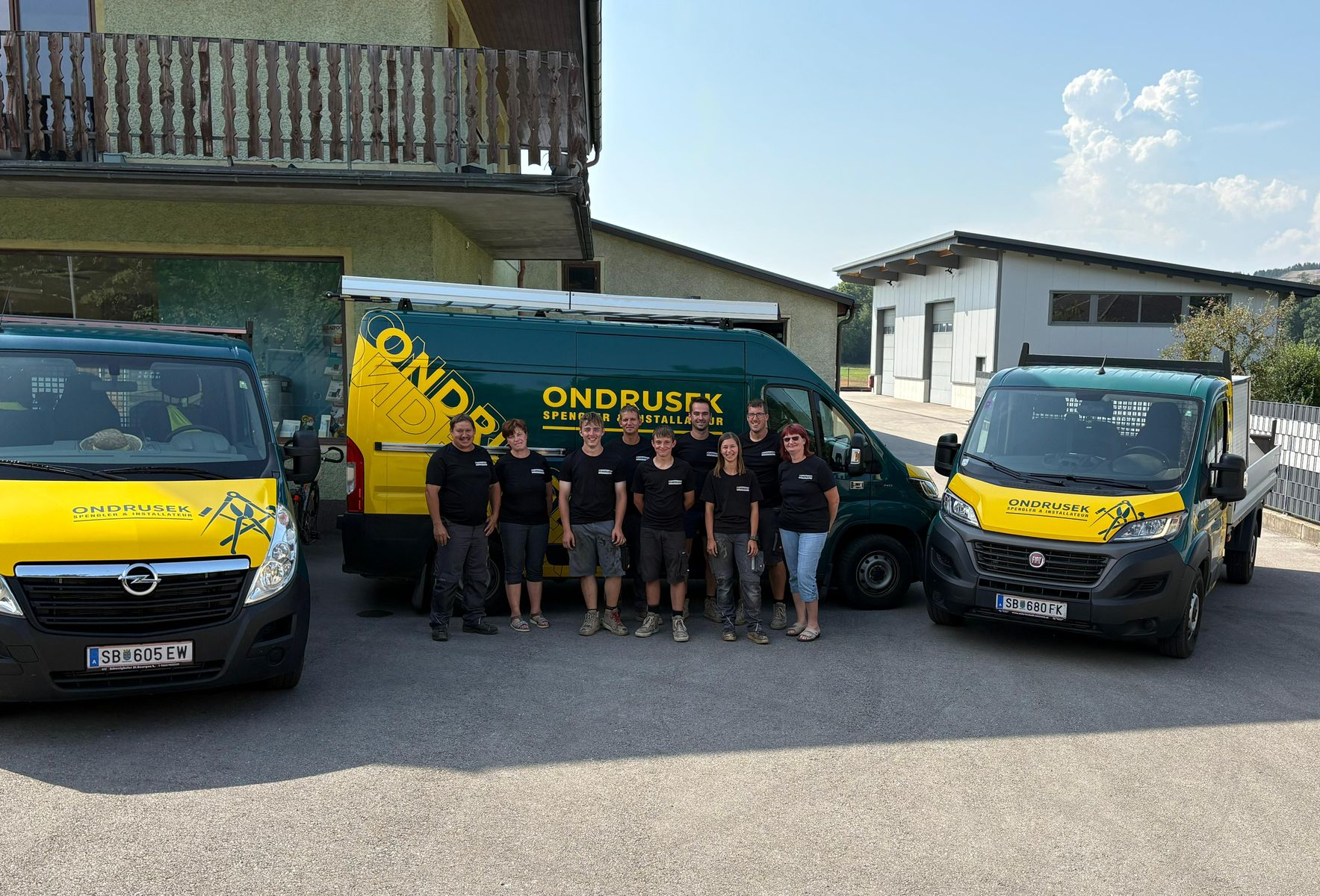 Gruppe von Menschen mit Firmenwagen, die vor einem Gebäude stehen.