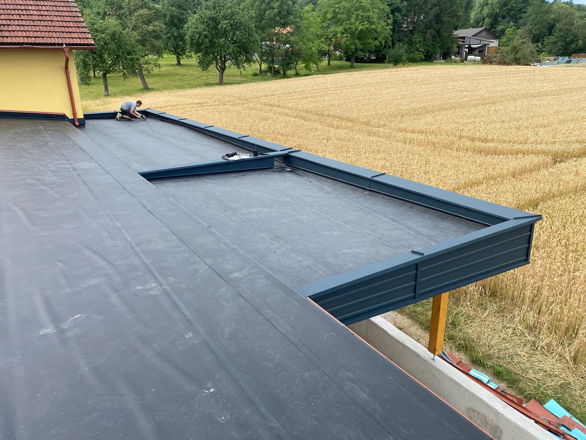 Eine Person arbeitet auf einem flachen, schwarzen Dach mit Metallrand vor einem Feld.