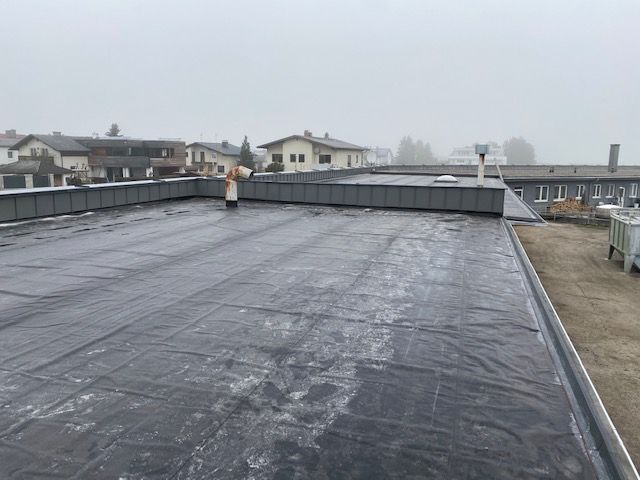 Flaches, schwarzes Dach eines Gebäudes in einer Stadt, bedeckter Himmel, einige Trümmer auf dem Dach.