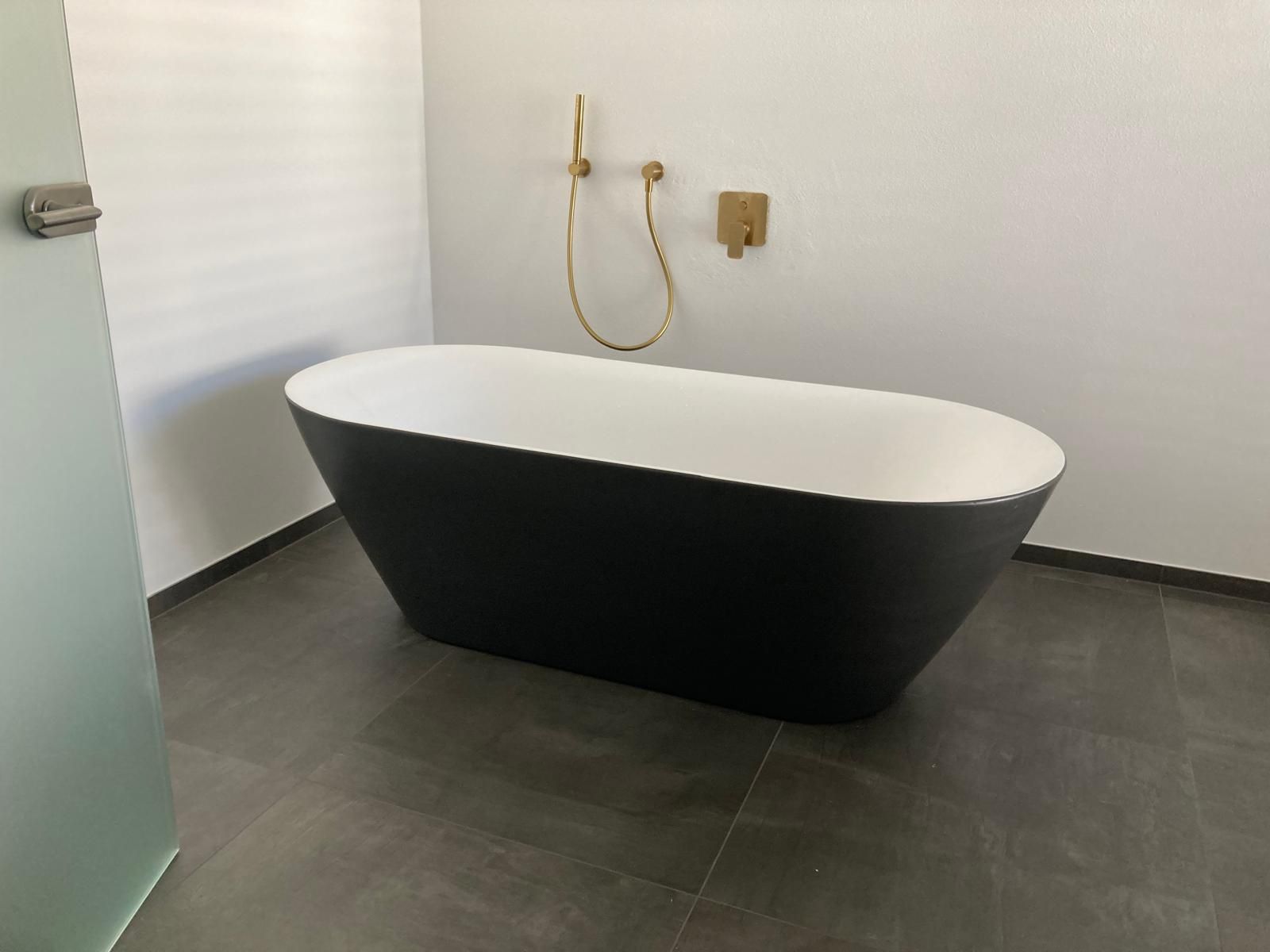 Schwarz-weiße ovale freistehende Badewanne mit goldenen Armaturen in einem modernen Badezimmer.
