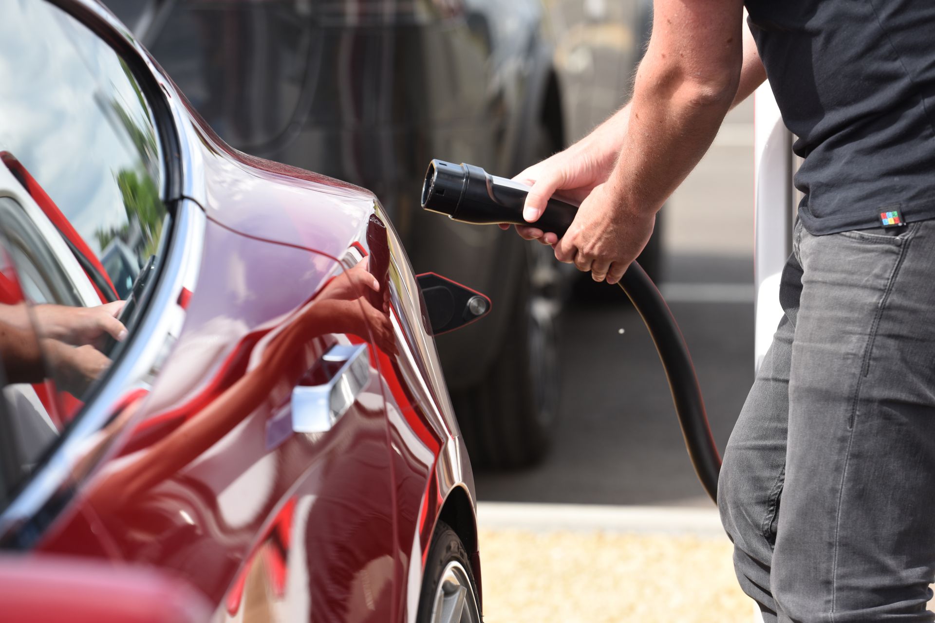 Une personne recharge une voiture électrique rouge à une station de recharge.