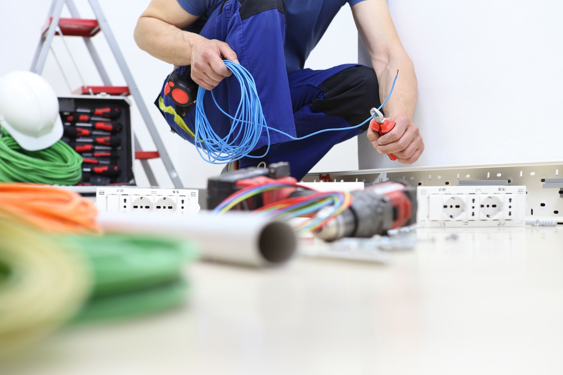 Professionnel réalisant des travaux de câblage électrique avec outils et équipements d’installation à proximité.