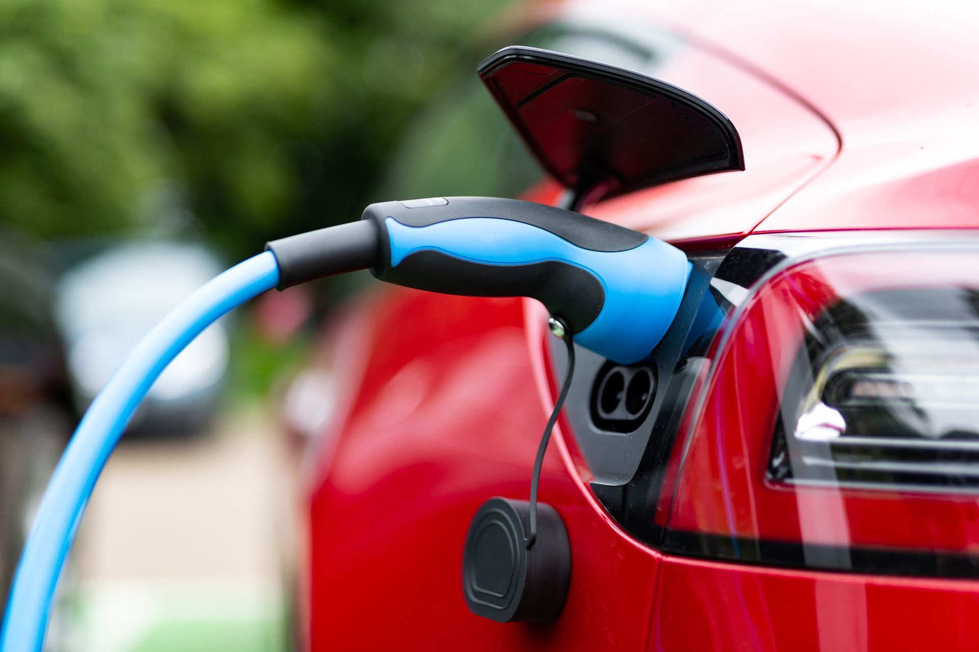 Prise de recharge bleue connectée à une voiture électrique rouge.