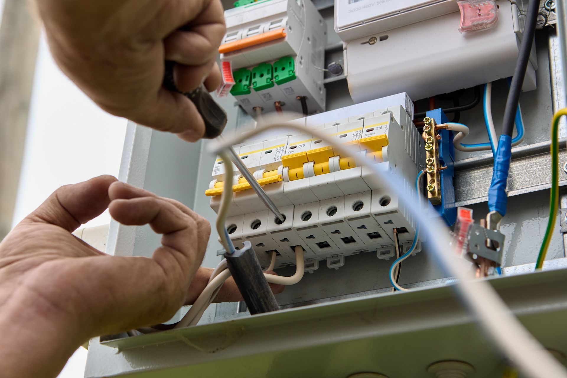 Un technicien raccorde des câbles dans un tableau électrique avec disjoncteurs et câblage.