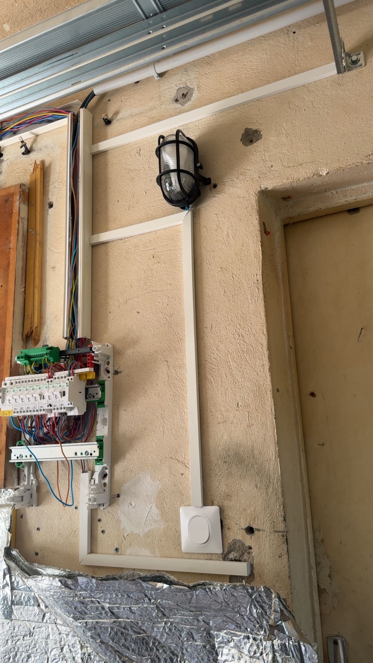 Mur extérieur en stuc beige avec un luminaire, une porte et un boîtier électrique en rénovation.