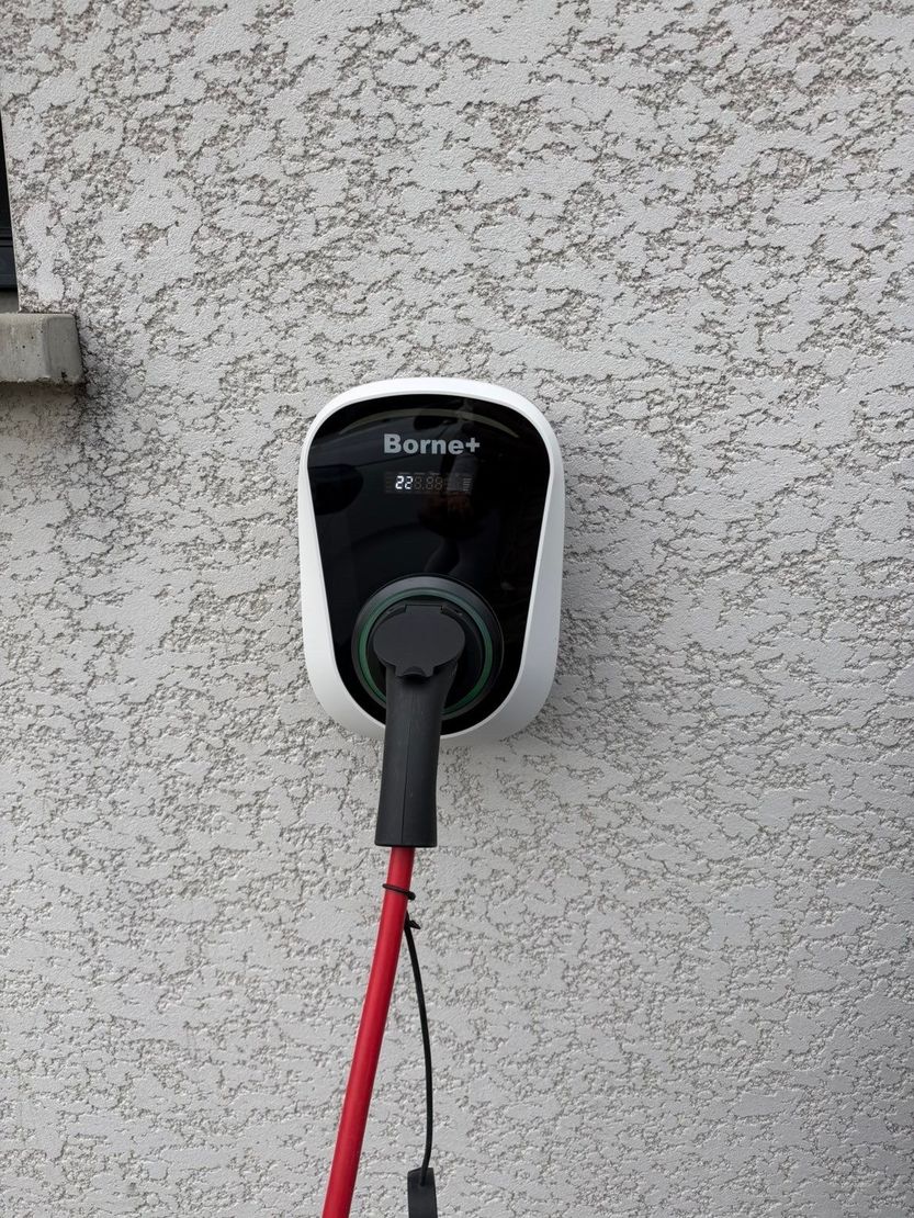 Borne de recharge résidentielle Borne +, fixée sur la façade d’une habitation avec câble de recharge branché.