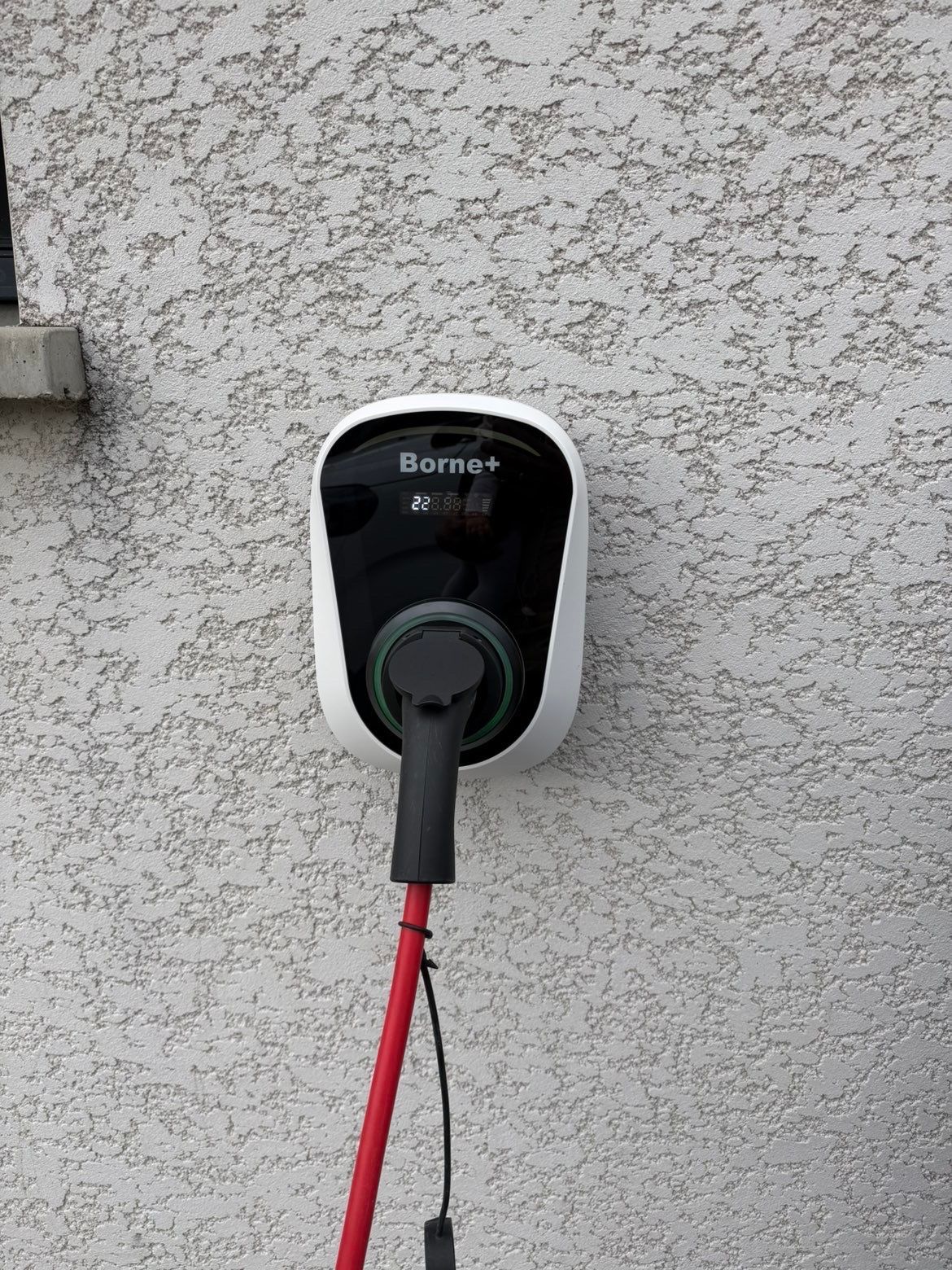 Borne de recharge résidentielle Borne +, fixée sur la façade d’une habitation avec câble de recharge branché.