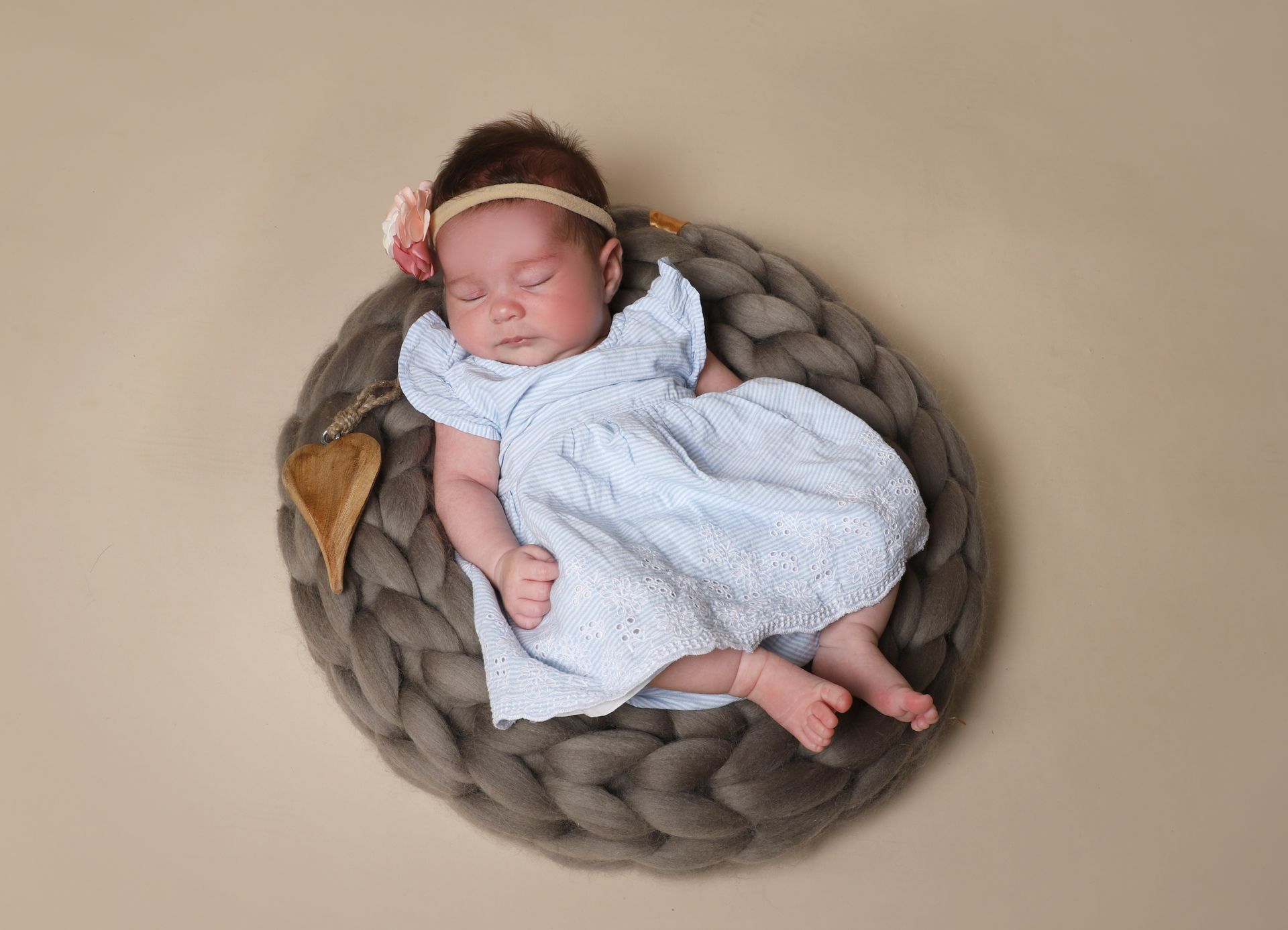 Ein Baby mit einem Blumenkranz liegt auf dem Bauch auf einer weißen Decke.