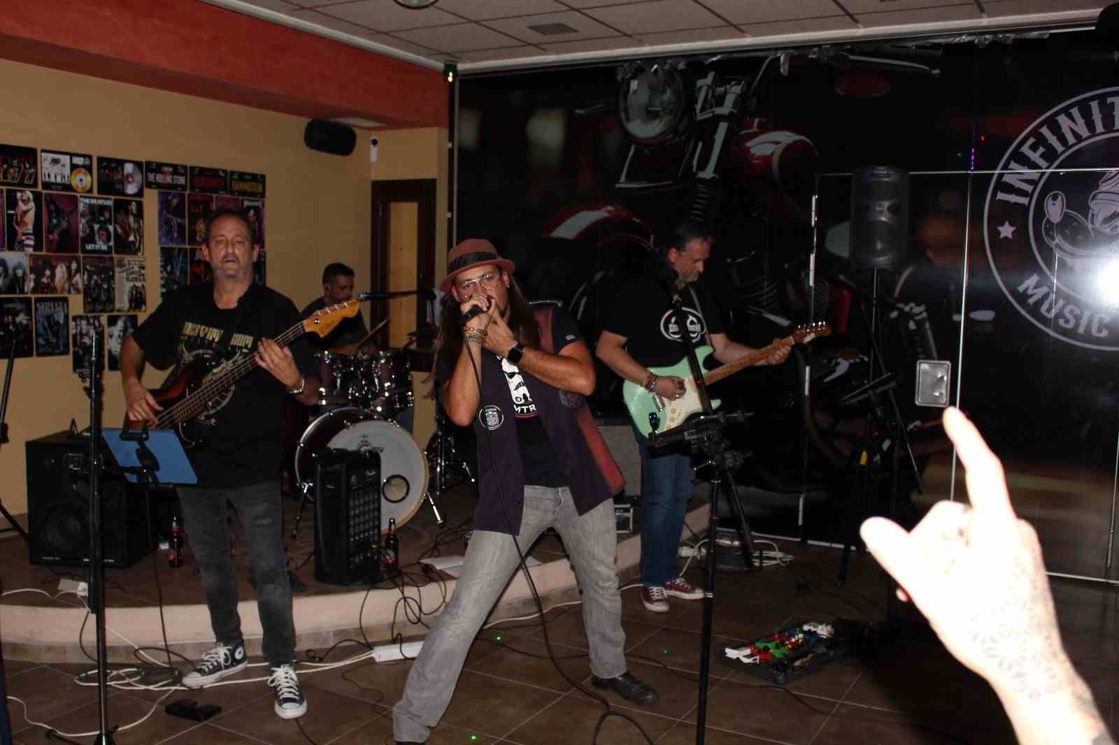 Banda tocando en el escenario en una sala de música con una mano en primer plano haciendo un gesto de rock and roll.