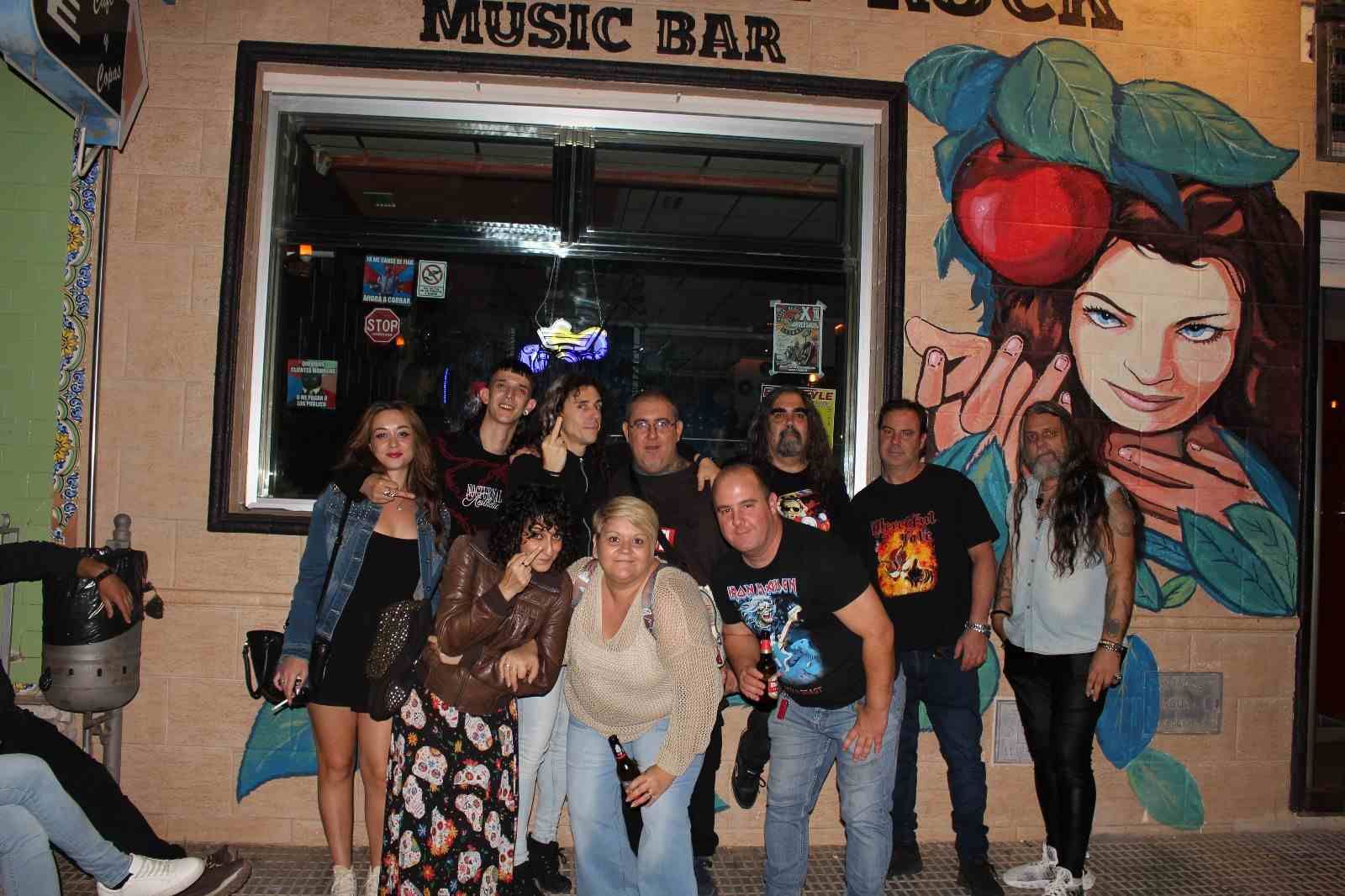 Grupo de personas posando frente a un bar de música rock con un mural de una mujer.