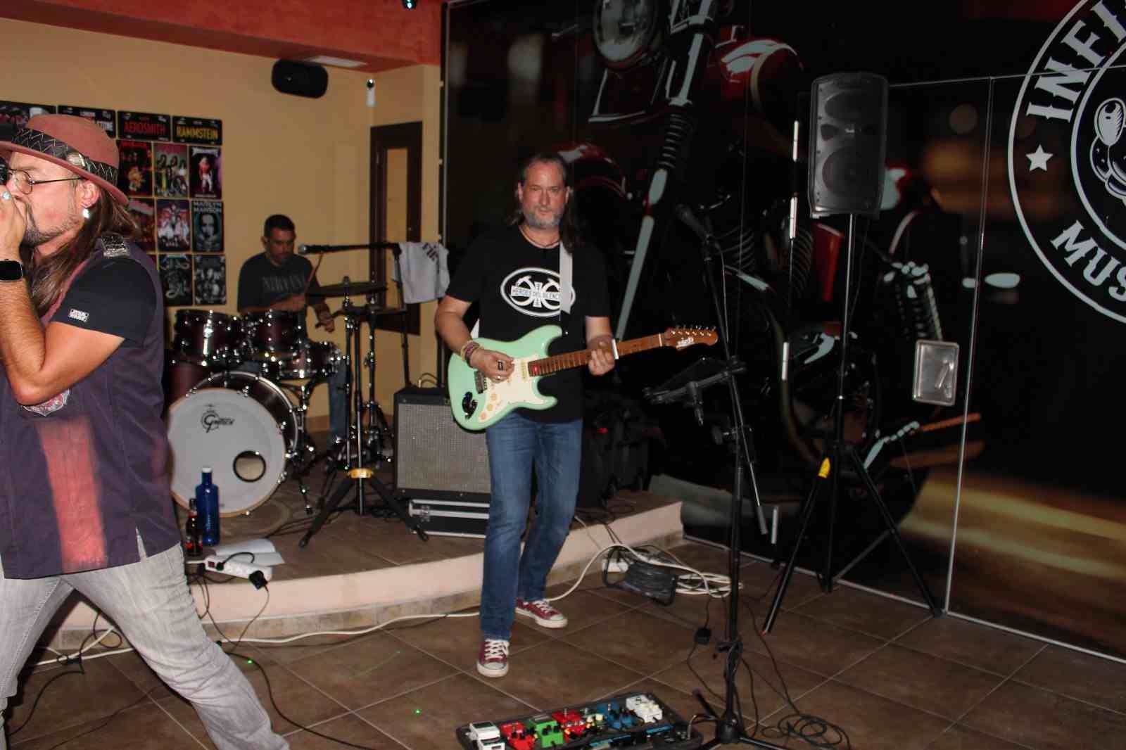 Banda tocando en vivo en un lugar con cantante, guitarrista y baterista.