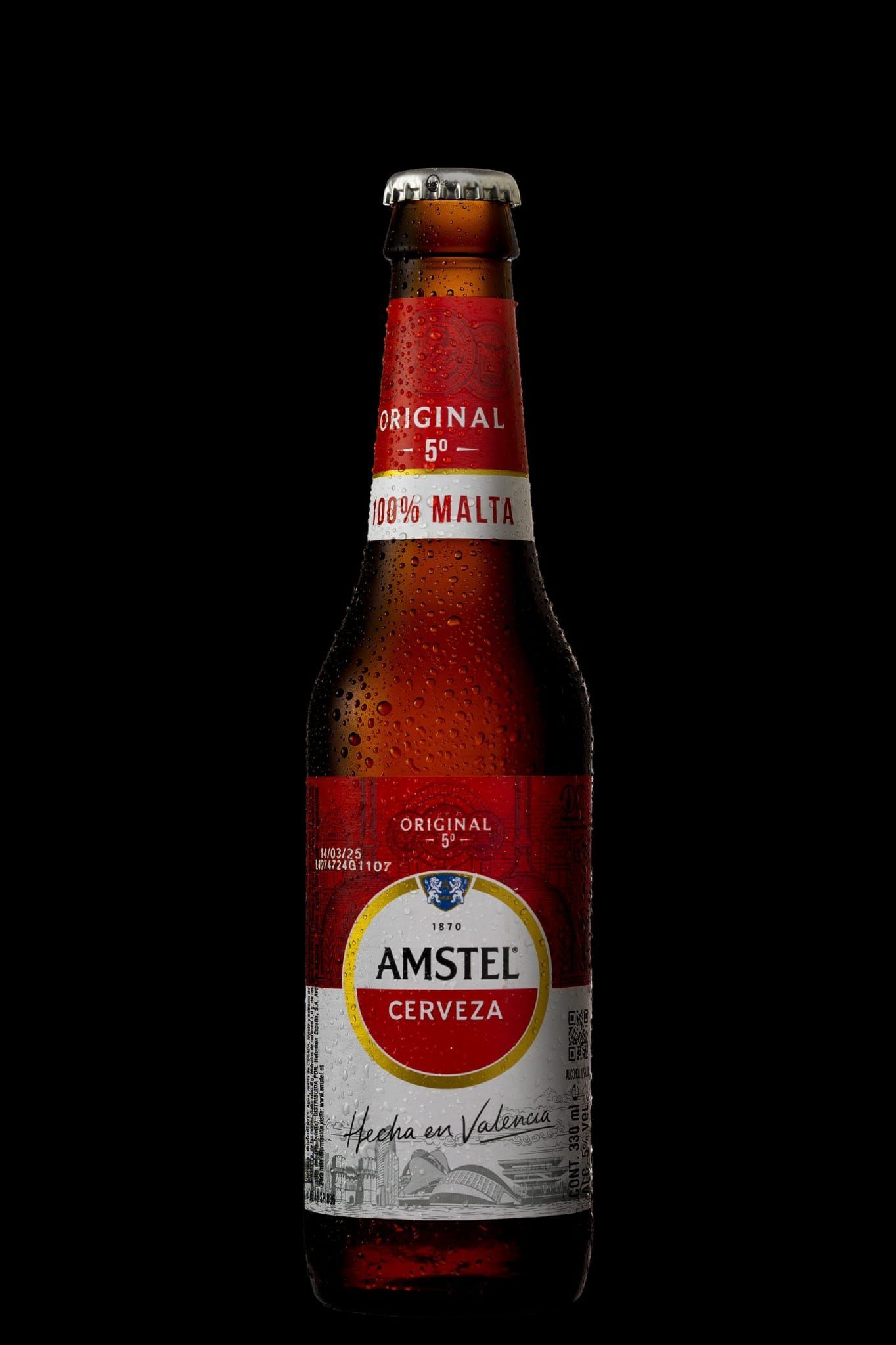 Botella de cerveza Amstel con etiqueta roja y blanca, sobre fondo negro.
