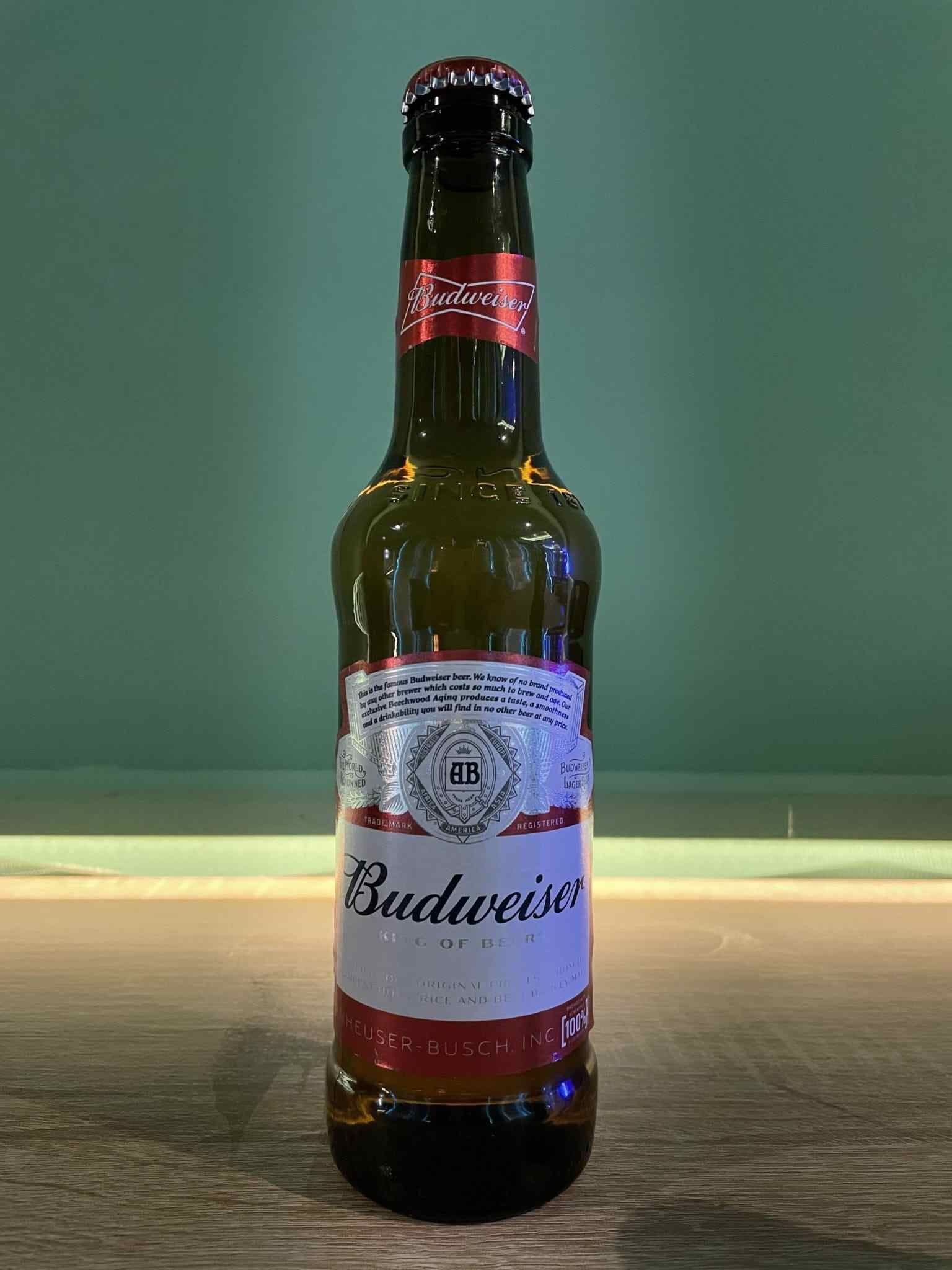 Botella de cerveza Budweiser sobre una mesa con fondo verde.