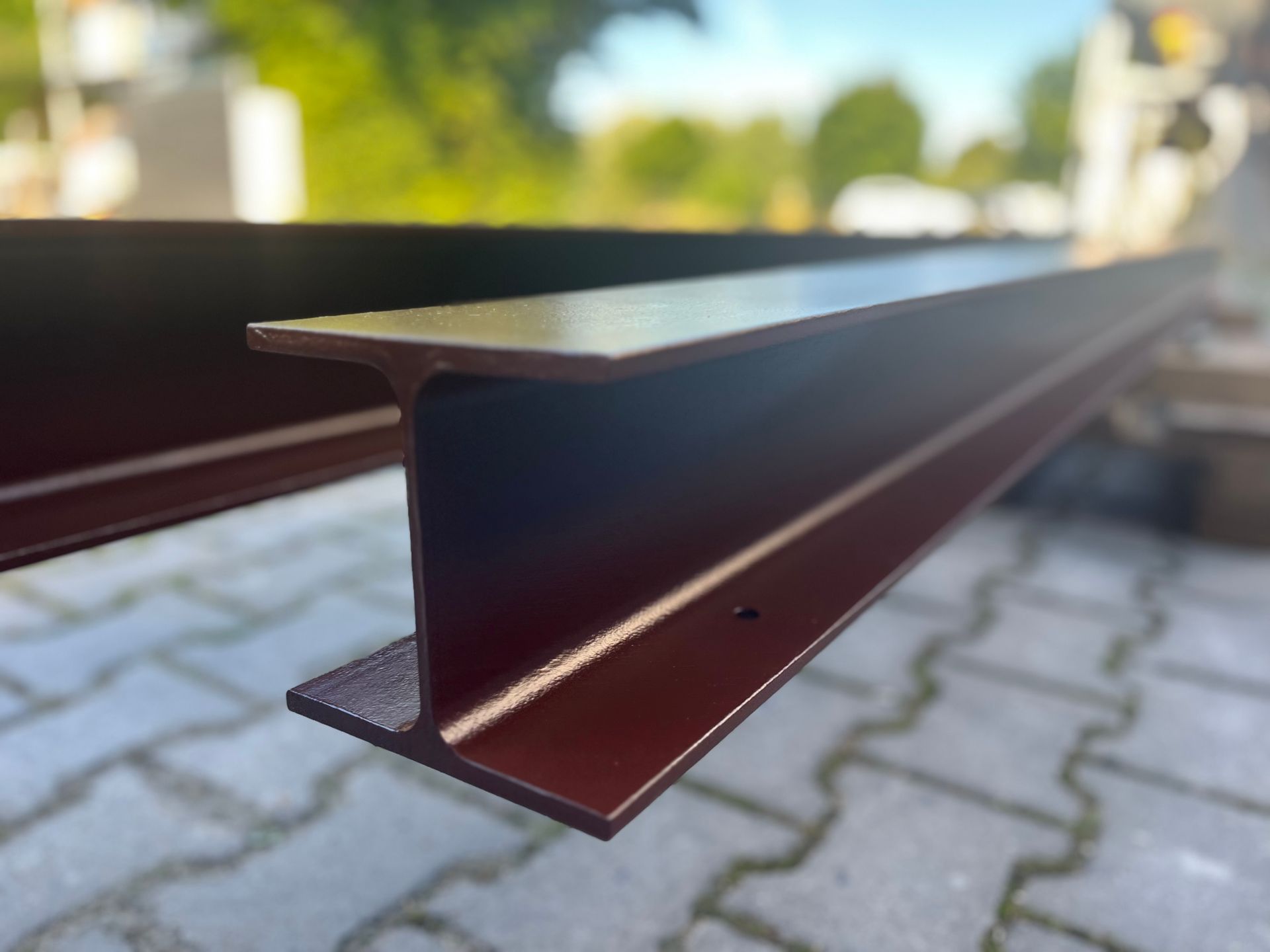Brauner Metall-I-Träger, im Freien auf einer gepflasterten Fläche.