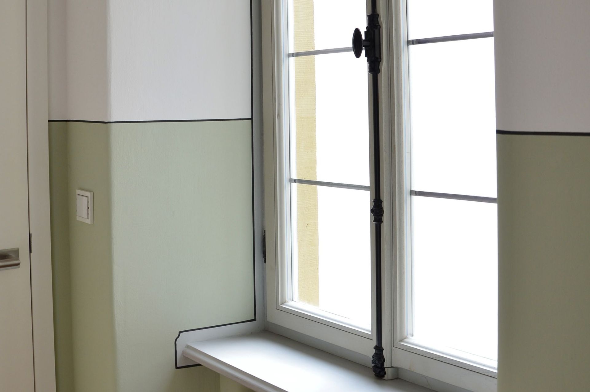 Fenster mit weißem Rahmen und hellgrünem Wandteil. Weiße Fensterbank und lichtdurchflutetes Fenster.