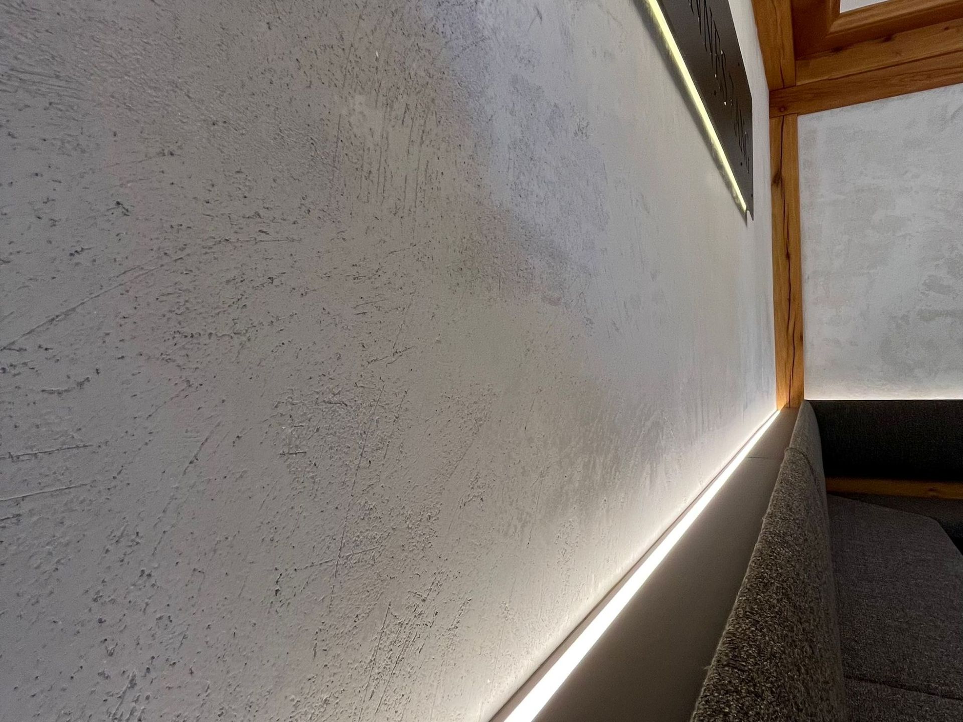 Strukturierte weiße Wand mit einem Lichtstreifen oben und unten, neben einer Ecke mit Holzrahmen.