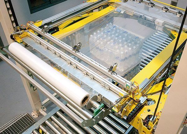 Una máquina está envolviendo botellas de plástico en una cinta transportadora.