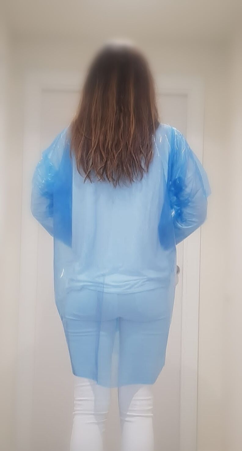 Una mujer lleva una bata de plástico azul y pantalones blancos.