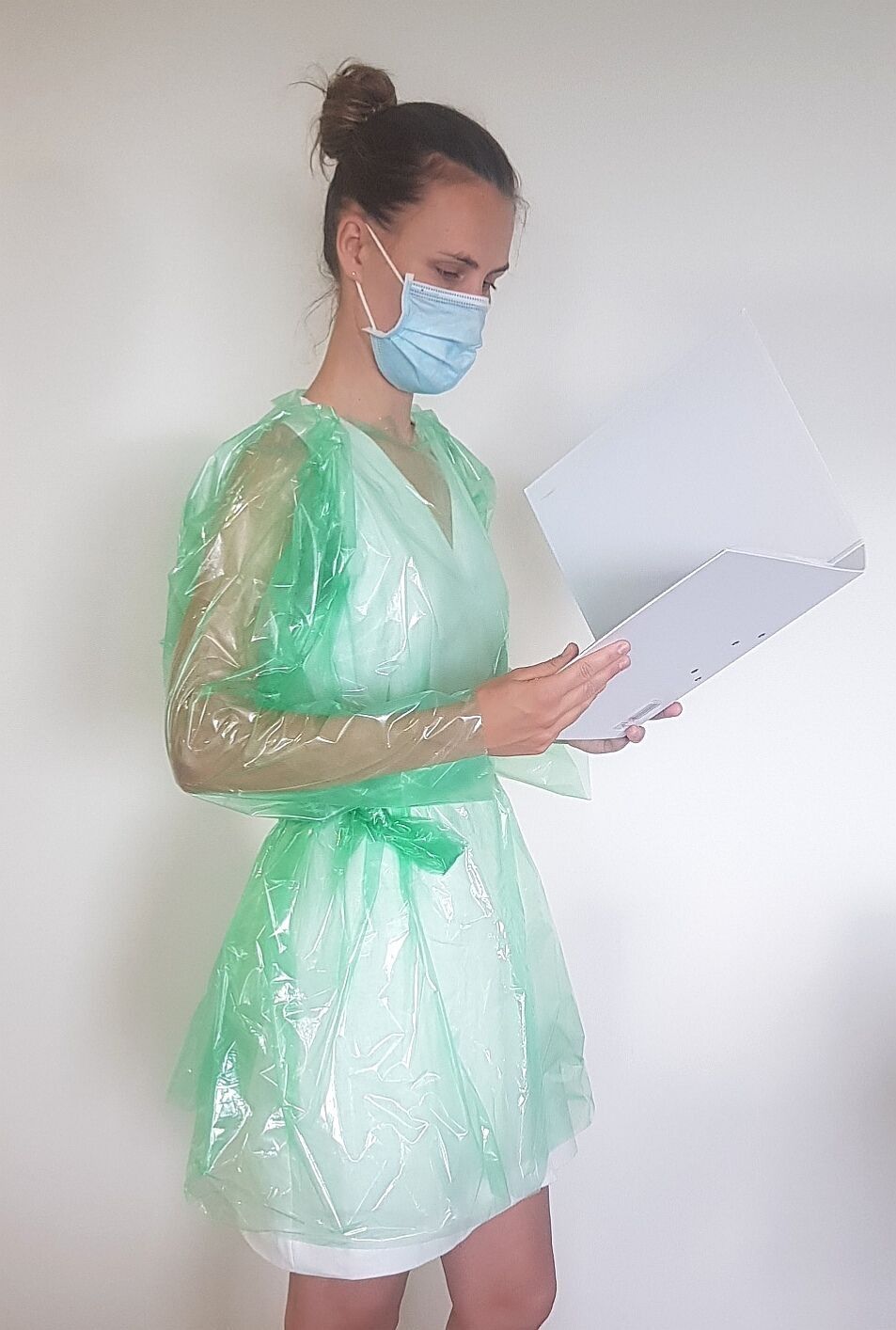 Una mujer que lleva una máscara y una bata de plástico verde sostiene un portapapeles.