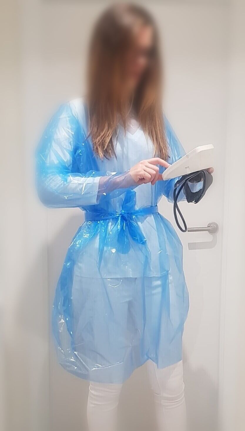 Una mujer con una bata de plástico azul sostiene una tableta.