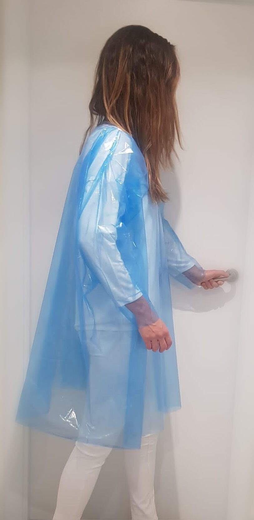Una mujer lleva una bata de plástico azul y pantalones blancos.