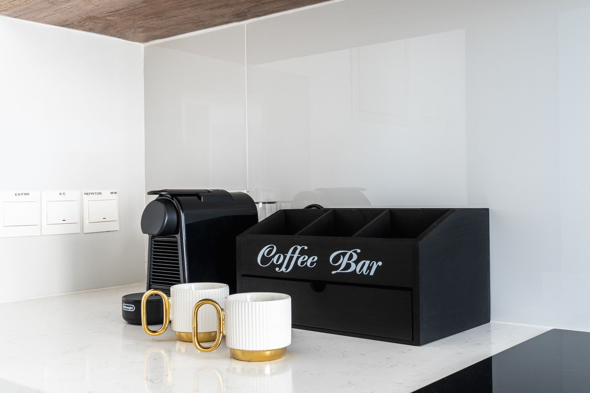 Coffee bar with a black espresso machine, mugs, and organizer on a white counter.