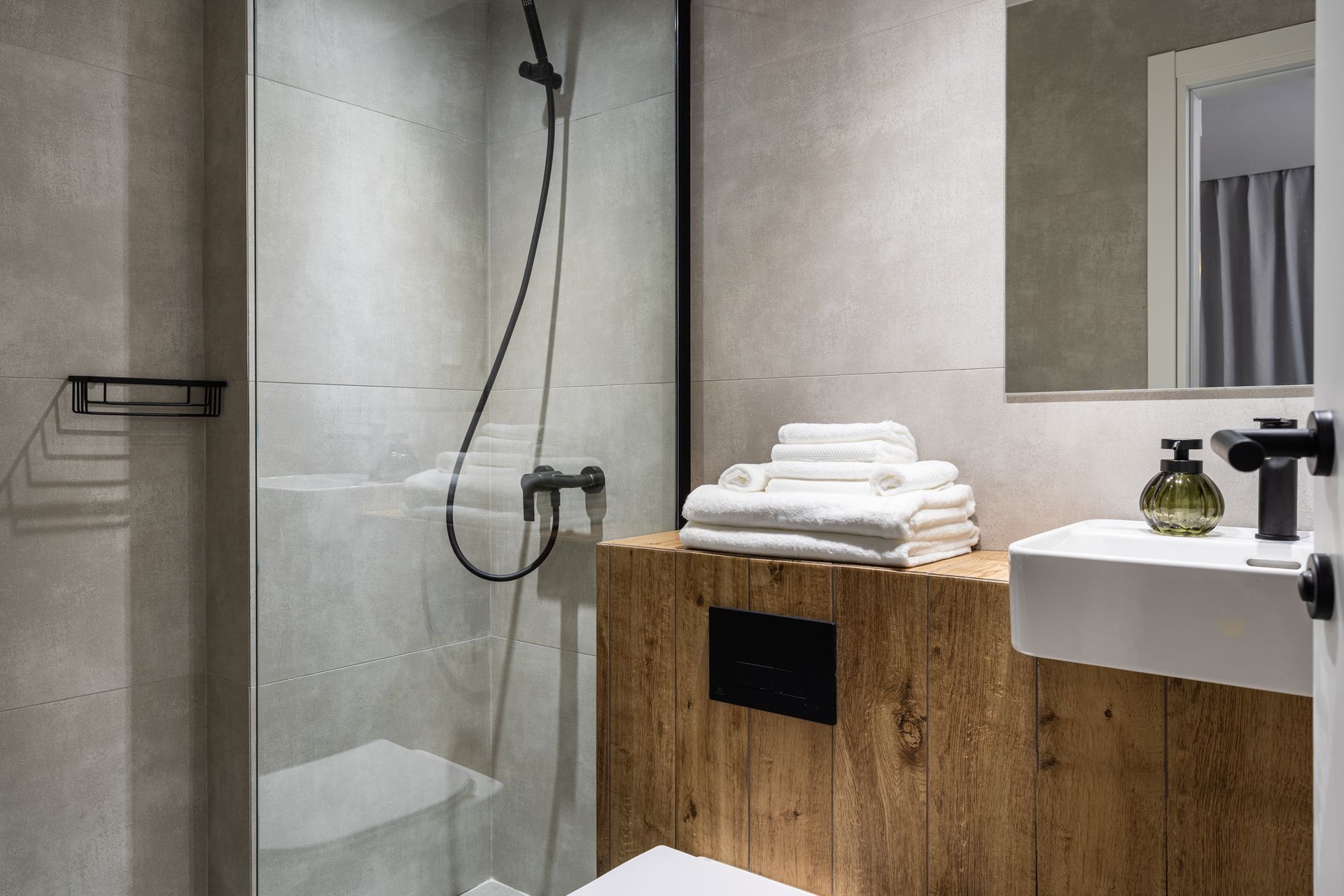 Modern bathroom with a glass shower, wooden vanity, white towels, and a square sink.