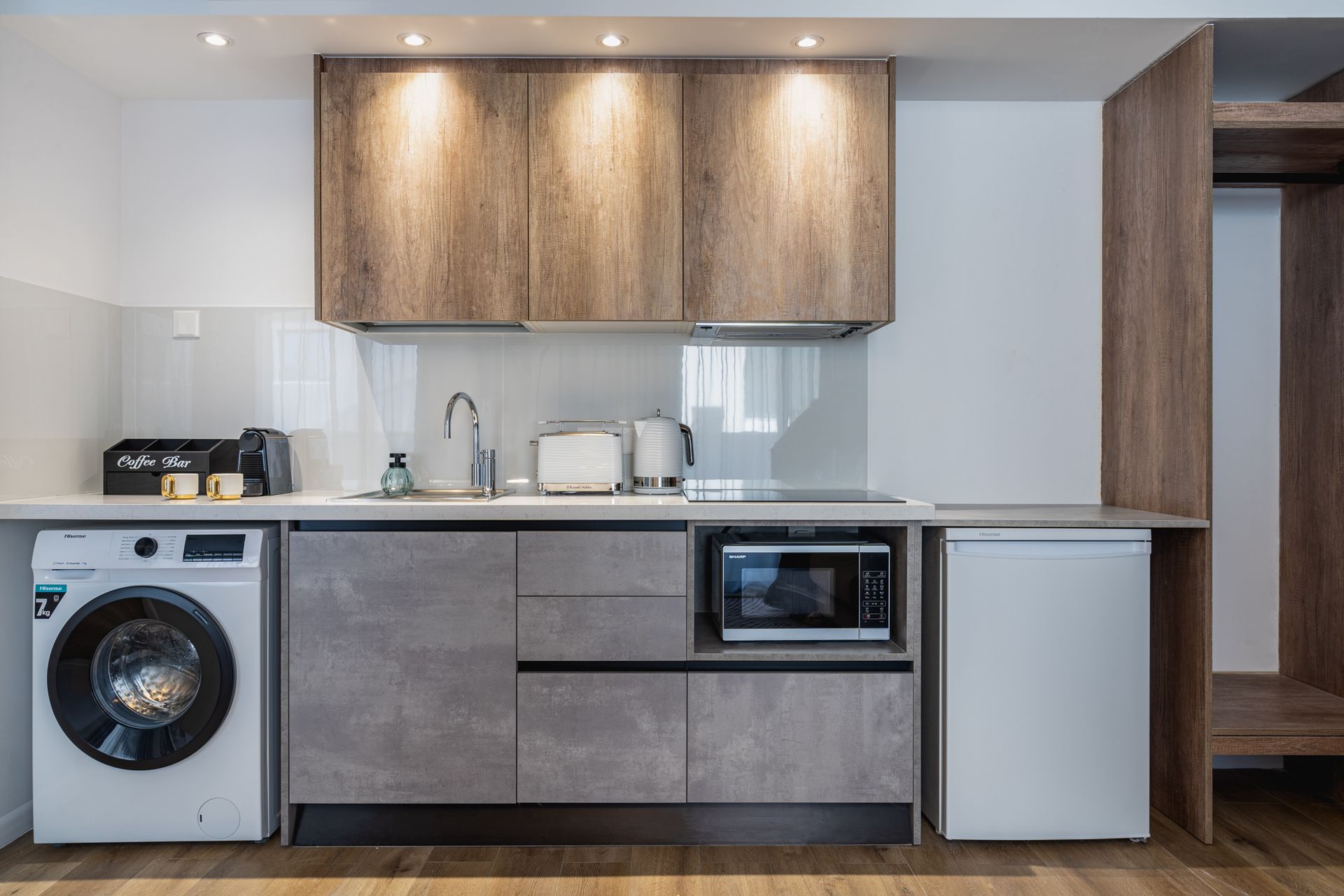 Compact apartment kitchen with washer, cabinets, microwave, and mini-fridge.