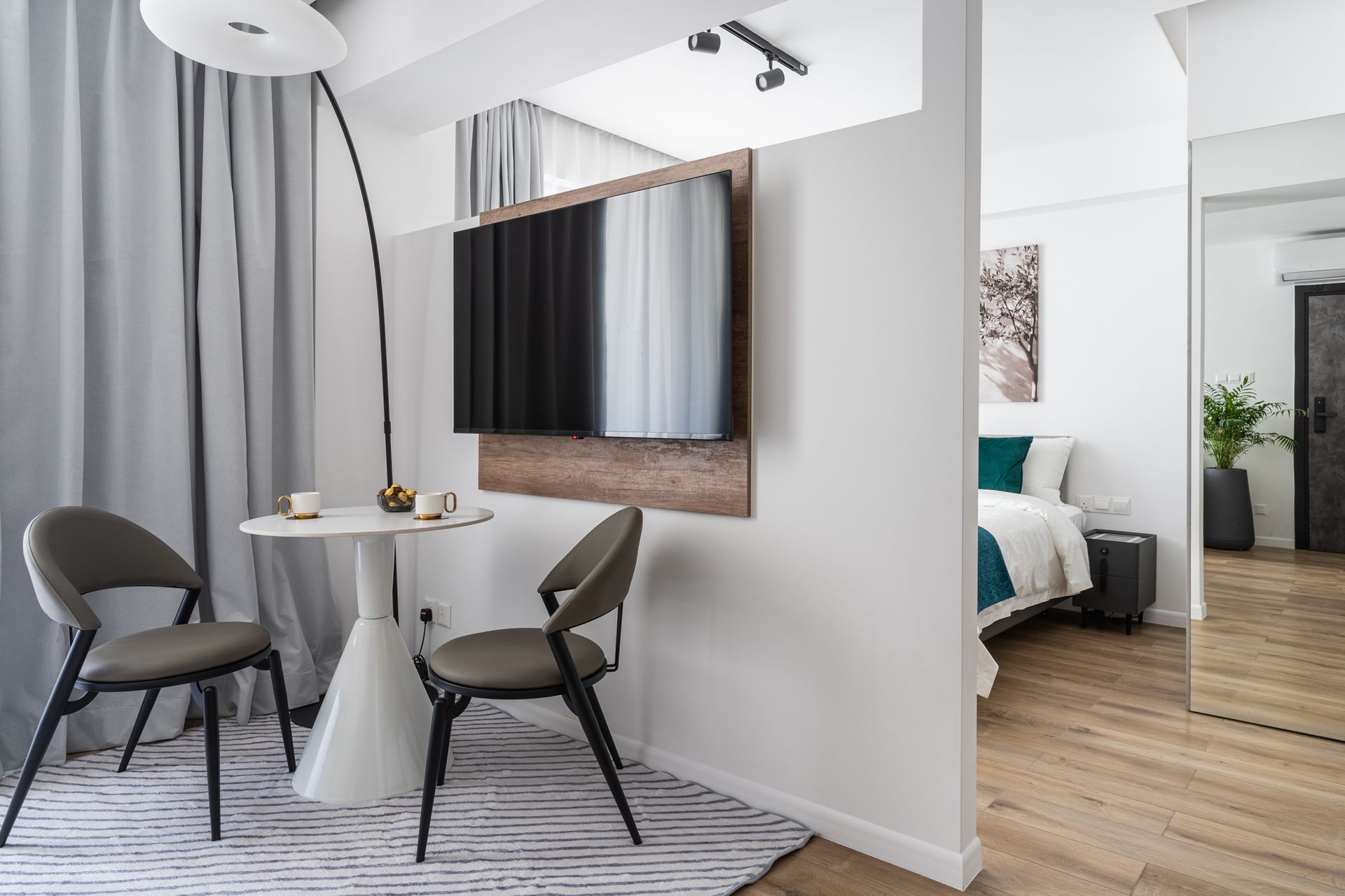 Small dining area with table and chairs next to a bedroom. A large TV is mounted on a wall.