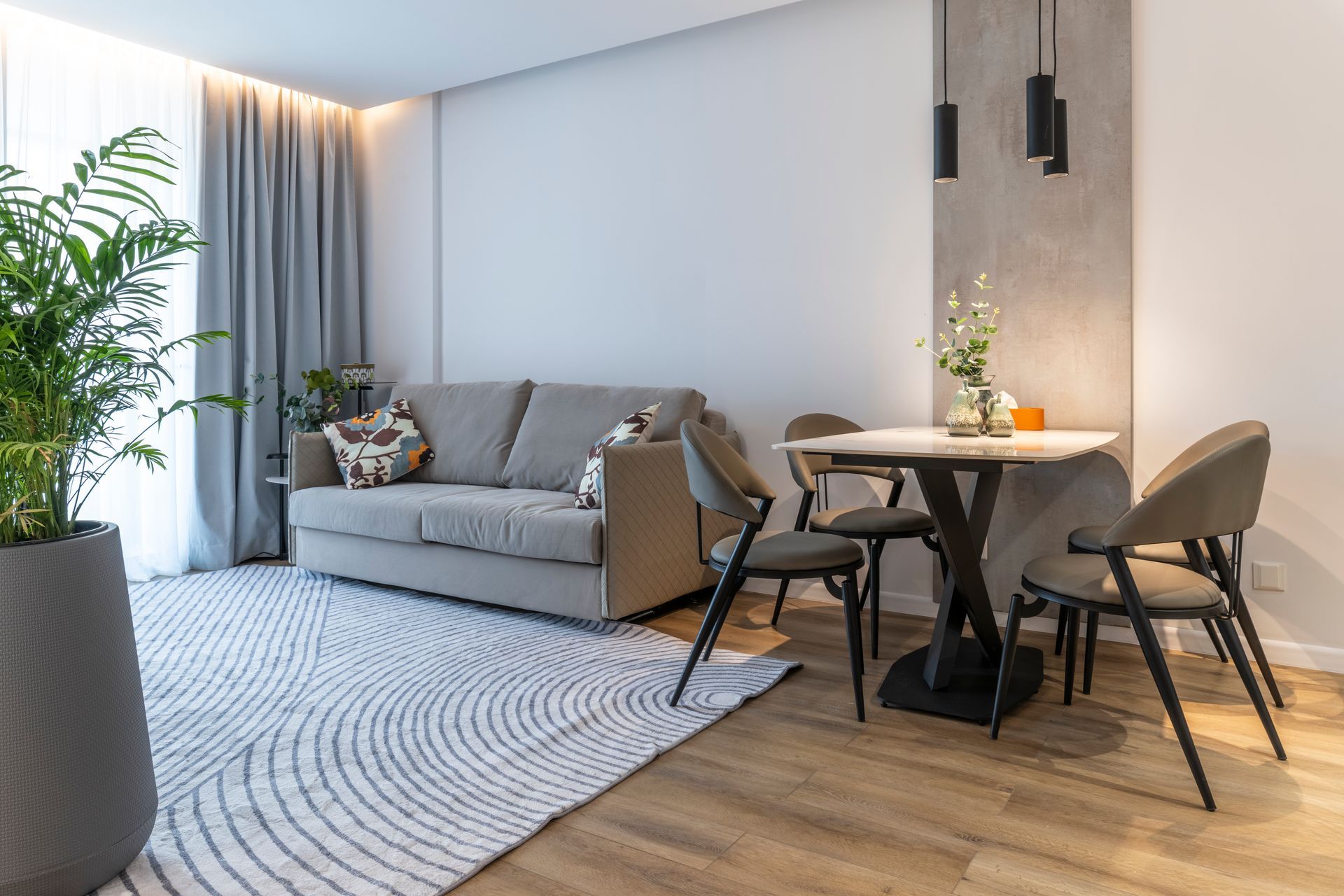 Living room with gray sofa, round table, chairs, plants, and patterned rug.