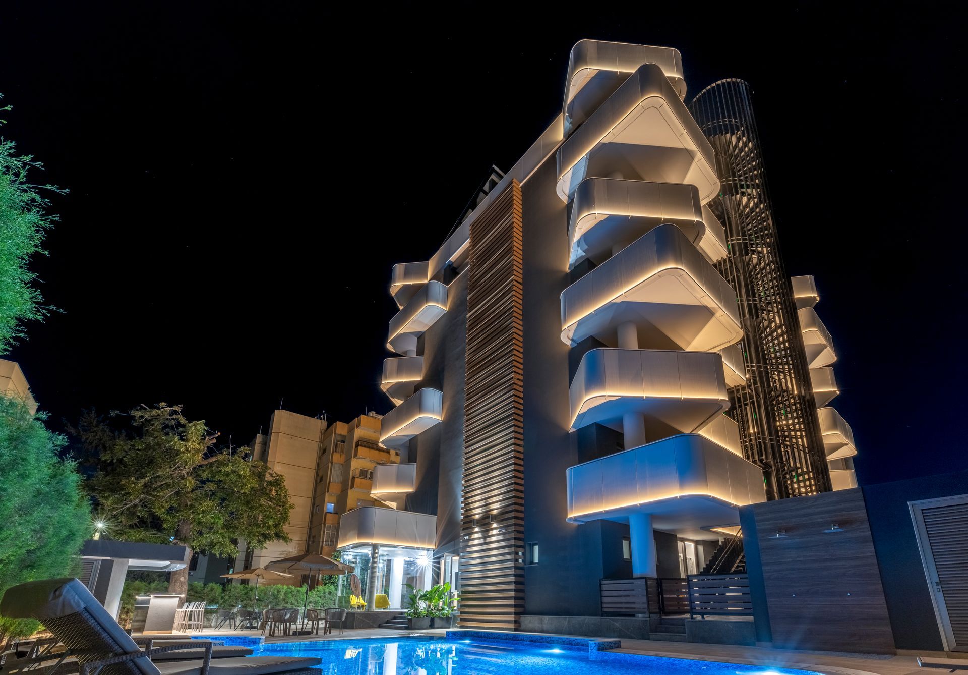 Modern building with lit balconies, pool at night.