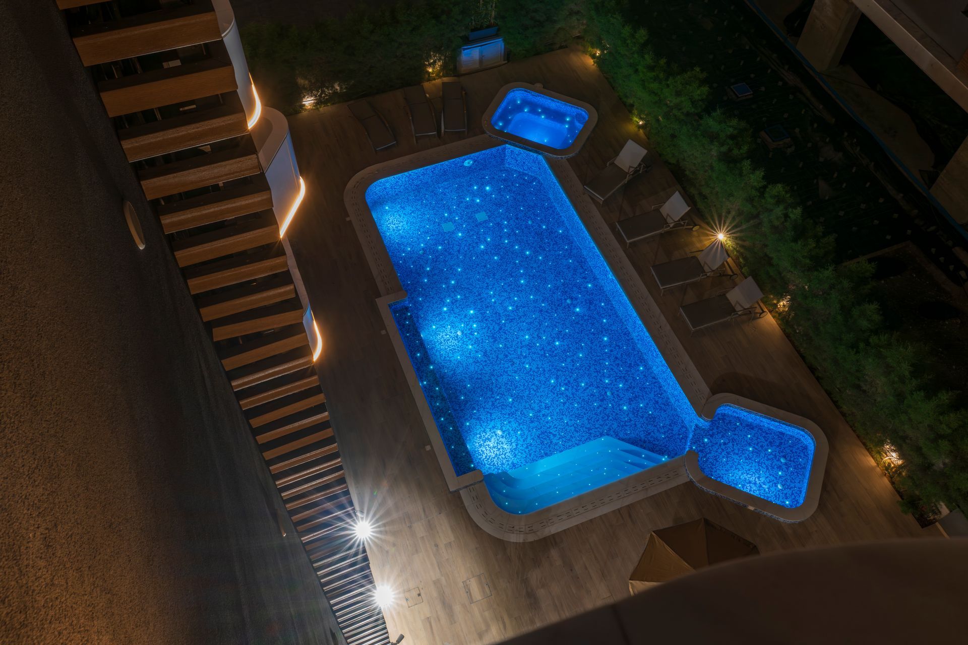 Night view of a rectangular pool and two connected jacuzzis, lit with starry blue lights.