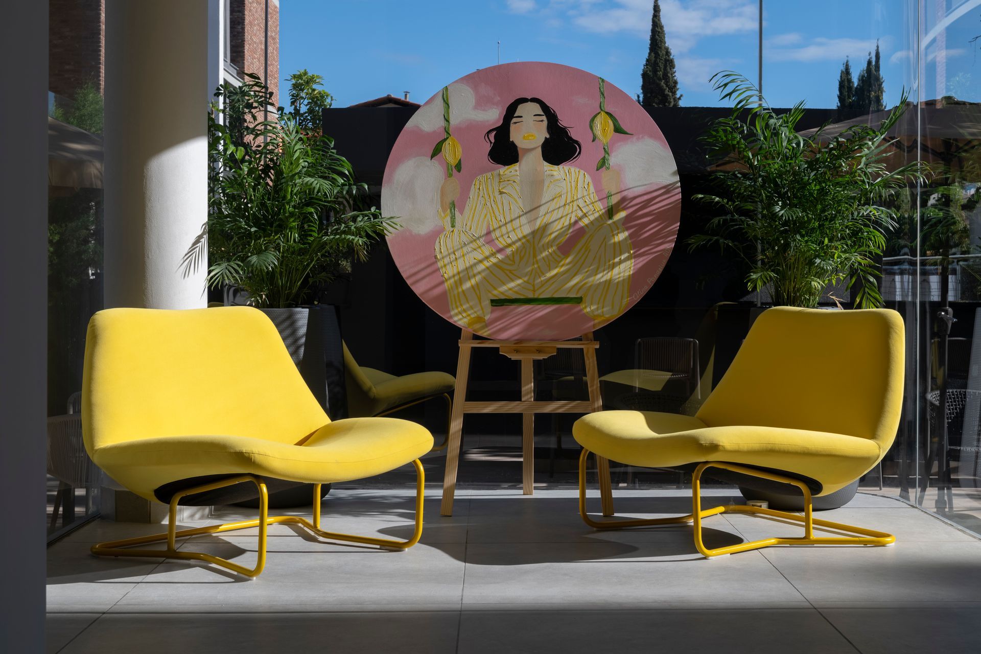 Two yellow chairs face artwork on an easel, set on a terrace.