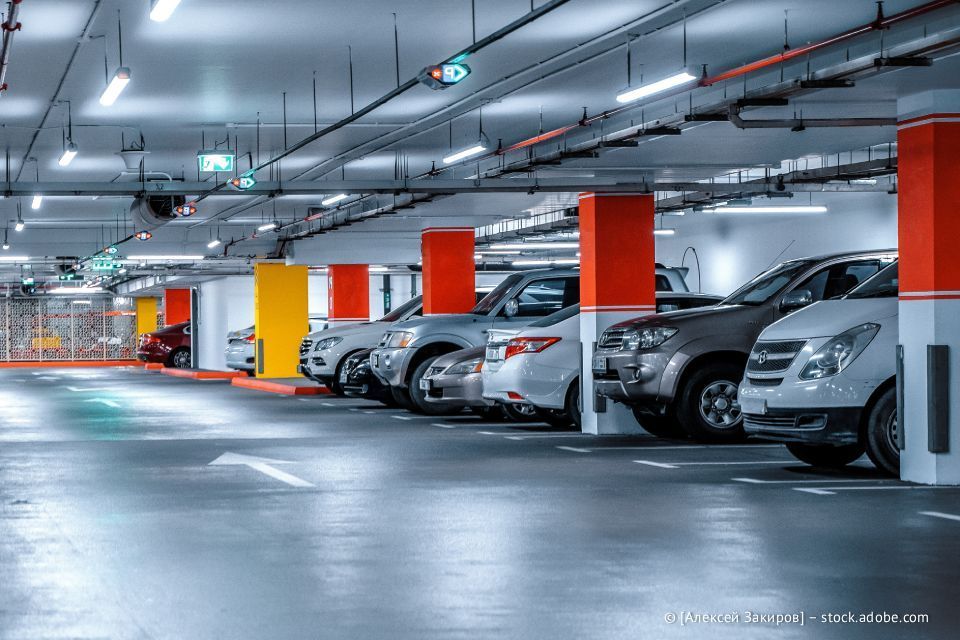 Autos parken in einem hell erleuchteten, mehrstöckigen Parkhaus mit roten und gelben Stützpfeilern.
