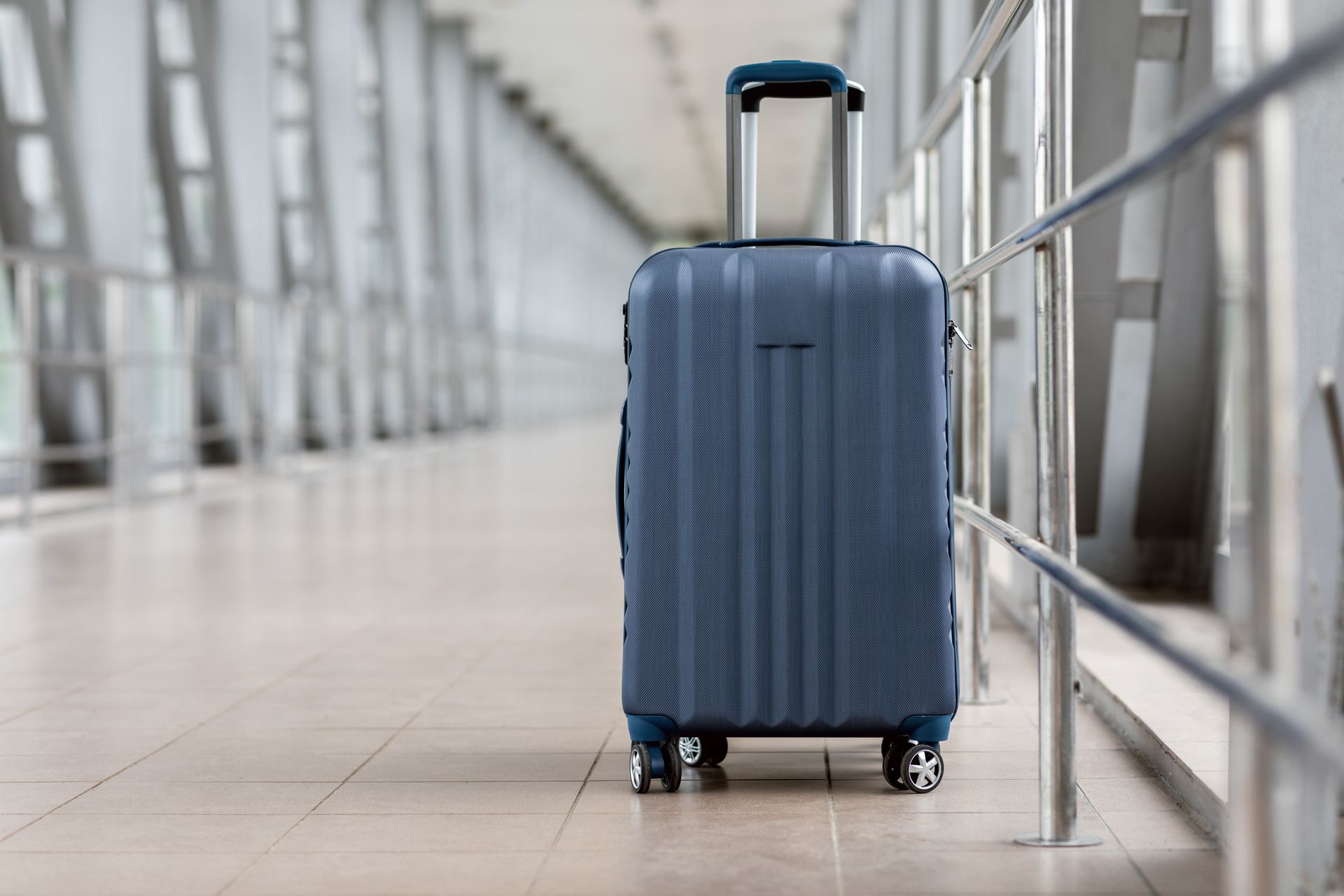 Une valise à roulettes bleue à coque rigide se trouve dans un couloir vide d'un terminal d'aéroport.