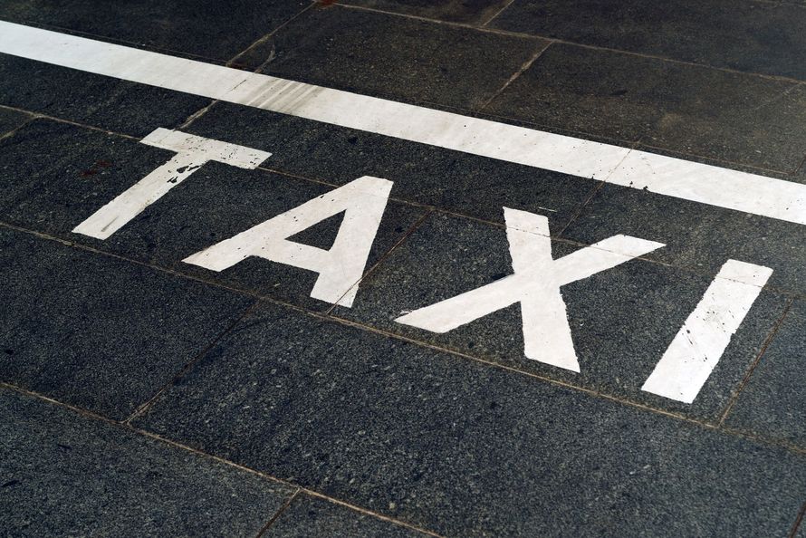 Le mot TAXI peint en lettres capitales blanches sur un sol carrelé sombre, avec une ligne blanche peinte au-dessus.
