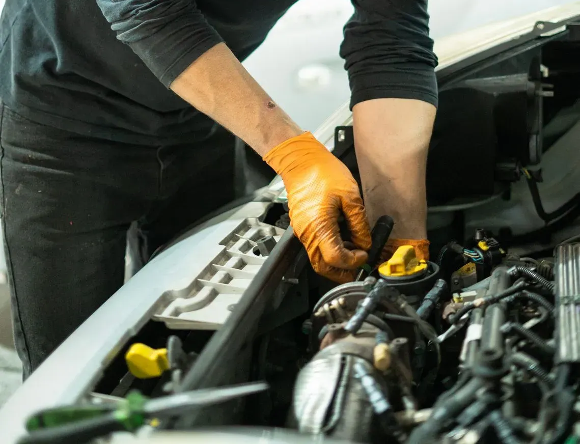 Mecánico con guantes naranjas trabajando en el motor de un coche, realizando tareas de mantenimiento.